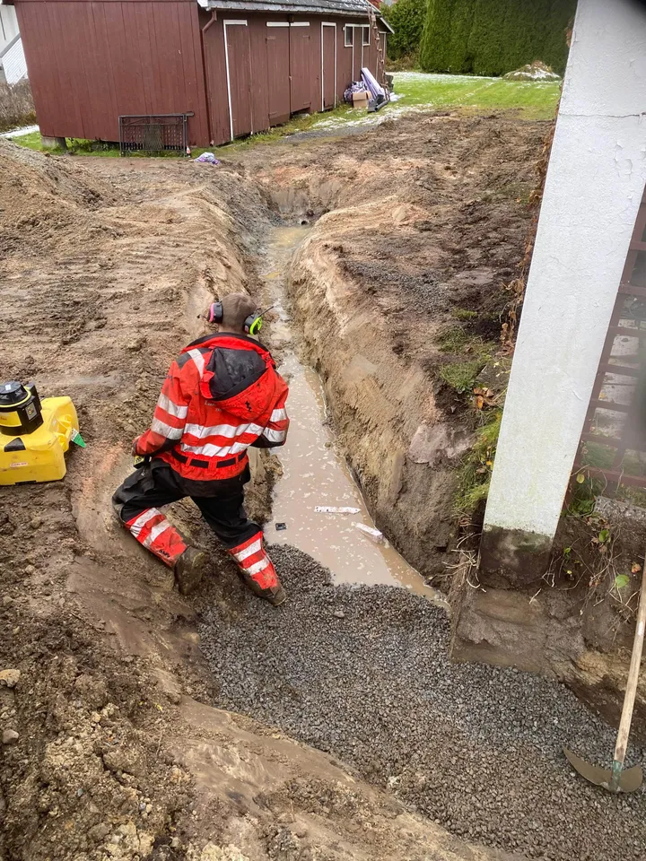 Anleggsarbeider i grøft langs grunnmuren under legging av ny drenering