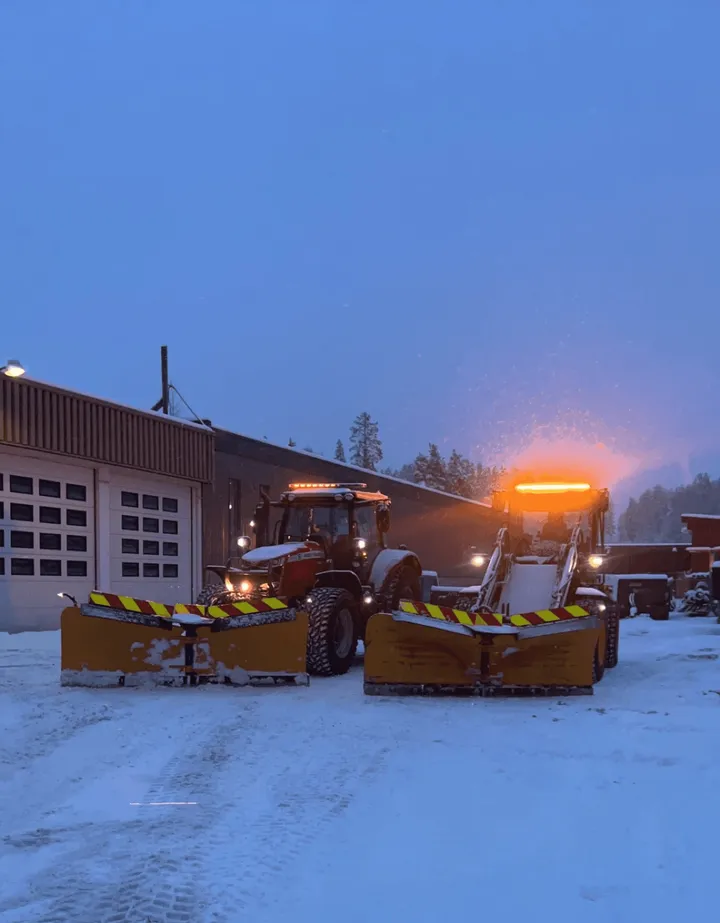 Traktor og hjullaster med brøyteskjær klare for brøyting en snørik morgen
