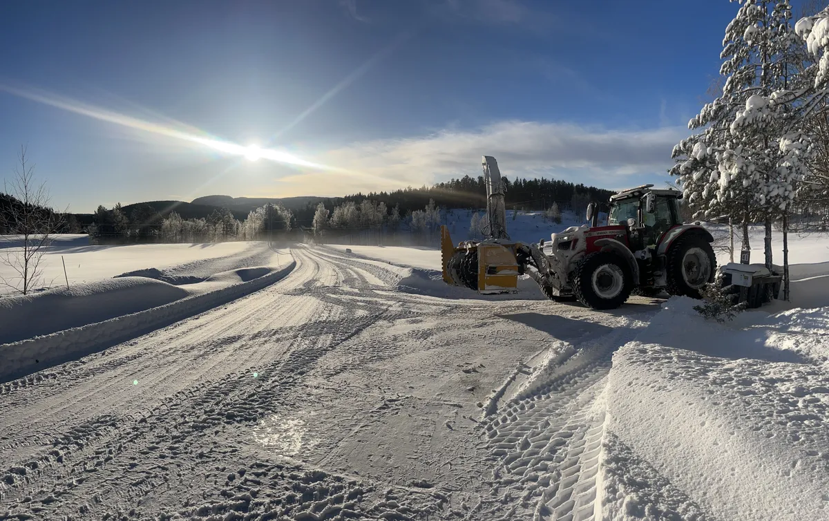 Traktor med snøfreser rydder en vei i vintersol