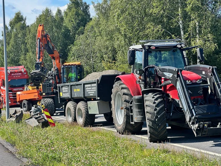 Gravemaskin, lastebil og traktor med henger i arbeid langs en vei