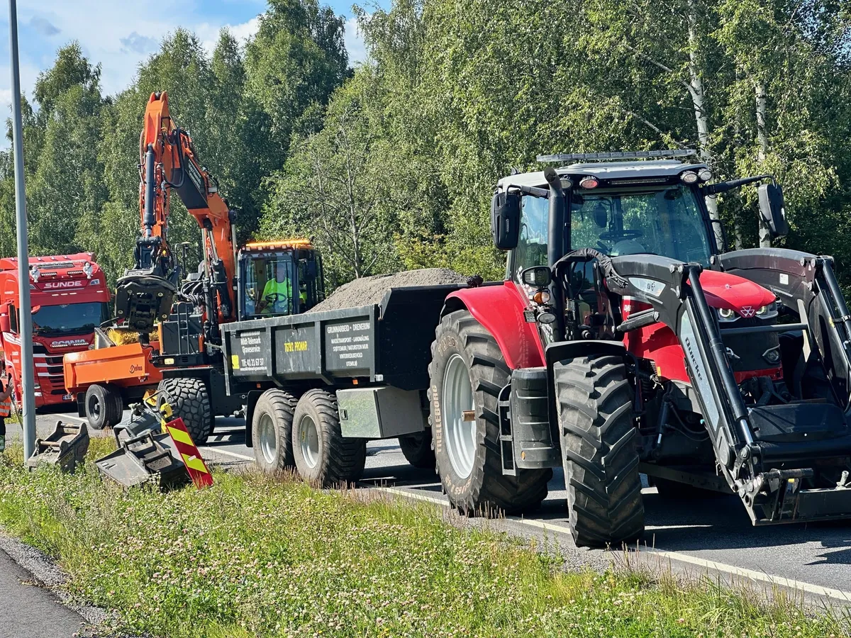 Gravemaskin, lastebil og traktor med henger i arbeid langs en vei